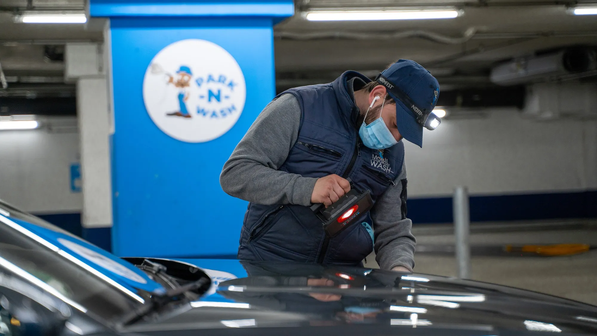 A Parknwash team member checks vehicle paint with a measuring device.