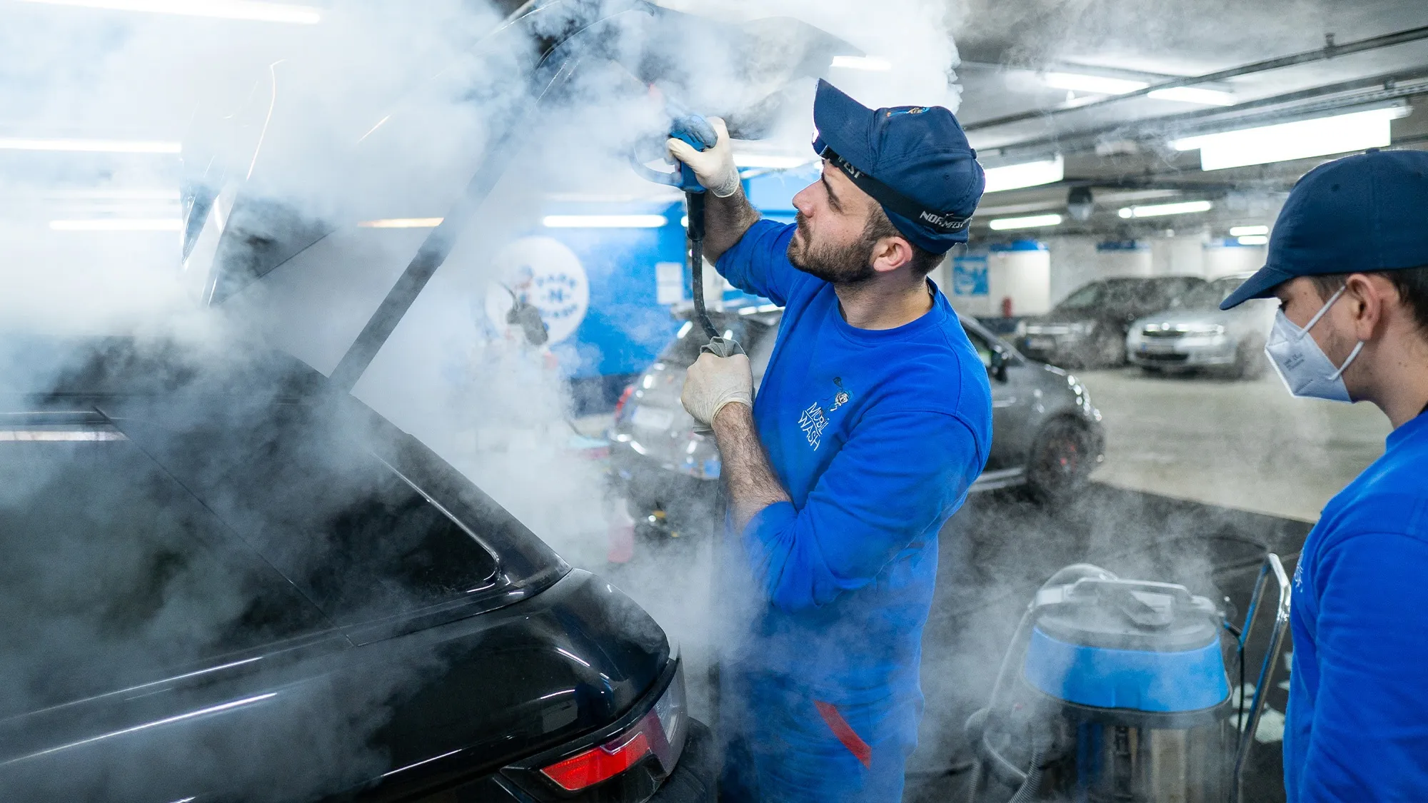 A Parknwash team member steam-cleans the open tailgate of a vehicle.